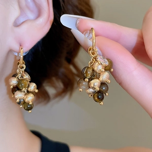 Close-up of golden geometric earrings with brown tiger eye stone and tassel detail