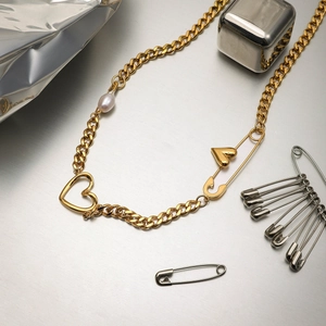 Detail of 18K gold paperclip necklace with heart pendant and freshwater pearl on metal surface