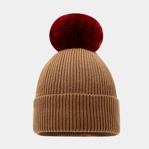 Macro detail of camel and burgundy ribbed knit texture on a winter beanie with pompom