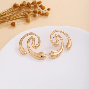 Detailed view of gold abstract spiral earrings on a minimalist white curved display