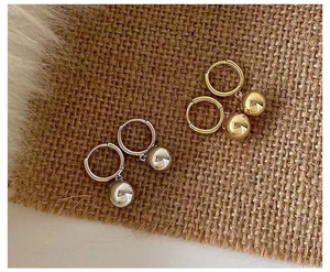 Makroaufnahme minimalistischer Kugelohrringe in Gold und Silber auf weichem Stoff