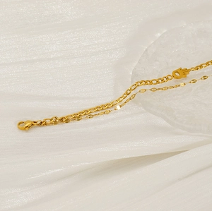 Detail of 18K gold-plated double-layer bracelet with Hamsa Hand pendant on white fabric
