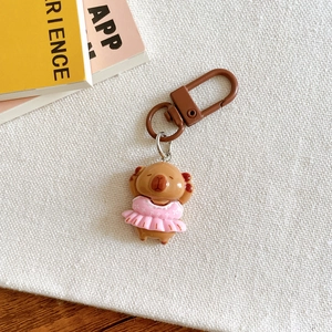 Detail of Capybara keychain in pink dress placed on white textured fabric for gifts
