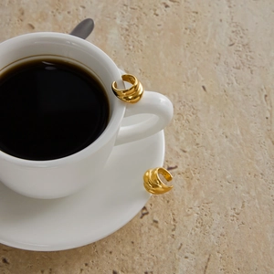 Detailed view of layered 18K gold stainless steel ear cuffs on a white coffee cup
