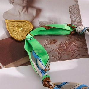 Detail of vintage 18K gold plated heart scarf buckle with green silk patterned scarf