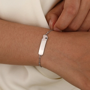 Close-up of a silver bear charm and polished name plate on a delicate chain bracelet