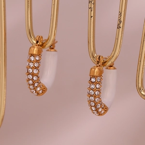 Macro detail of U-shaped gold plated earrings with white enamel and pavé cubic zirconia