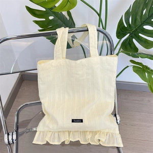 Detail of cream canvas tote bag featuring vertical ribbed texture and ruffle trim