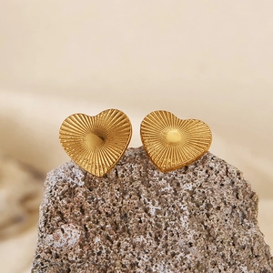 Macro detail of gold heart earrings with radial texture on a natural stone surface