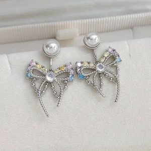 Macro shot of silver bow knot earrings with colorful zircon stones and round pearls