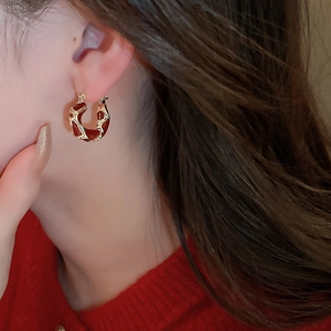 Close-up of vintage U-shaped earrings with red enamel and gold trim on model