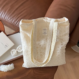 Close-up of cream lace embroidery tote bag with square fabric patch on wooden table