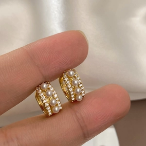 Macro detail of gold hoop earrings featuring three small pearls and pavé cubic zirconia