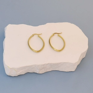 Close-up of golden hoop earrings with diagonal texture engraving on a stone display