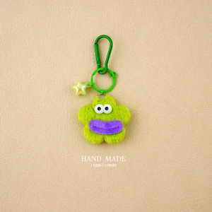 Close-up of a green plush monster keychain with a yellow star charm and a metal clip hook