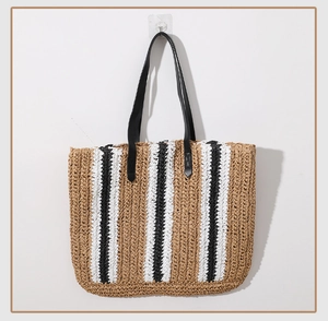 Detail of handwoven striped straw tote bag featuring black PU leather straps and sharp textures