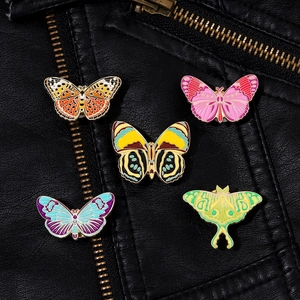 Set of five colorful butterfly and moth enamel pins on a black leather jacket texture