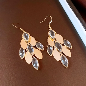 Detailed close-up of gold-plated leaf-shaped drop earrings with clear crystal stones