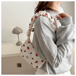 Close-up of white corduroy shoulder bag with red strawberry prints and ruffled strap