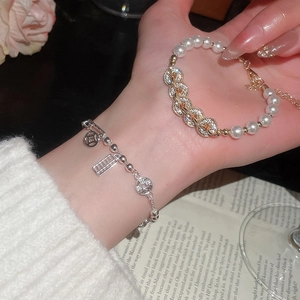Detail showing two layered bracelets with pearl, zircon, and lucky coin charms on a wrist