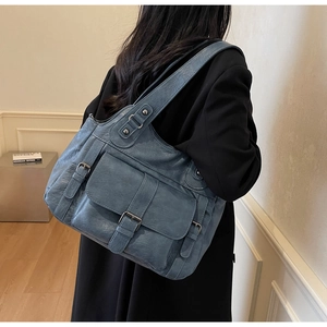 Detail of grey-blue leather tote bag with buckle pockets on a model in a black blazer