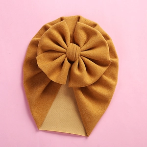 Detailed flat lay of ginger yellow knit baby turban hat with oversized bow on pink background