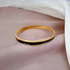 Minimalist gold titanium steel bangle with black enamel inlay on elegant fabric background