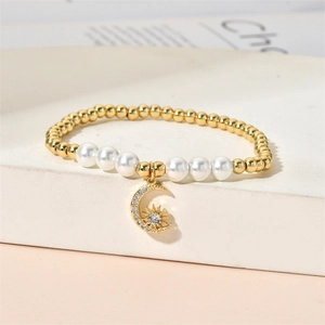Detail of beaded bracelet featuring gold beads, pearls, and a moon sun charm on a white stand