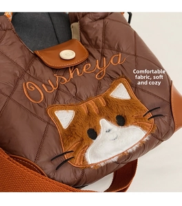 Close-up of brown quilted nylon tote bag with orange cat plush patch and magnetic buckle