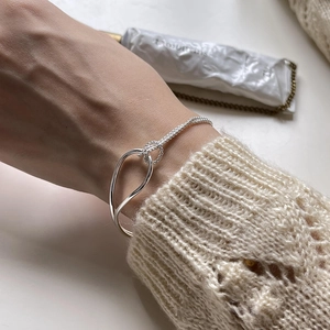 Detail of minimalist S925 silver knot bracelet with woven metal texture on wrist