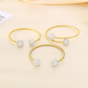 Close-up of golden steel wire woven bangles with crystal-encrusted silver ball ends
