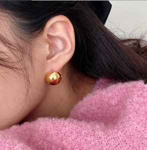 Detail of polished golden spherical earrings worn with a soft pink fleece sweater