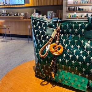 Green translucent tote bag with scale patterns and cute pretzel charm on wooden table