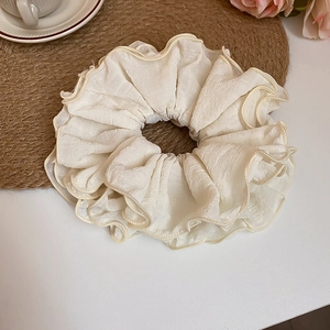 Close-up of cream ruffled fabric scrunchie on woven mat with soft floral background