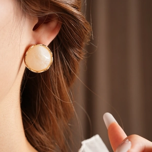Close-up of French vintage round wrinkled cream earring with a hammered gold metal frame