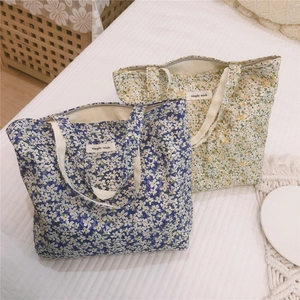 Dettaglio di borse in tela floreale con cerniera ed etichetta Simple Wish su letto bianco