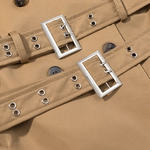Detail of khaki trench coat featuring double belts with silver buckles and twill fabric