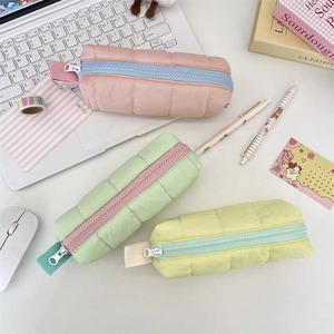 Three quilted puffer pencil cases in pastel colors arranged on a desk with stationery