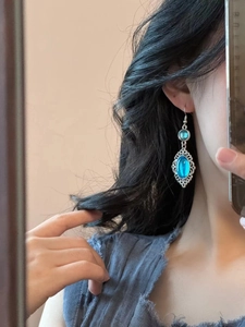 Close-up of vintage resin drop earrings with bright blue stones worn by a woman