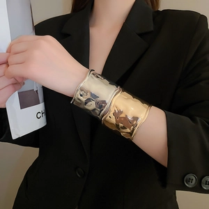 Detail showing gold and silver textured wave cuff bracelets on a model wearing black suit