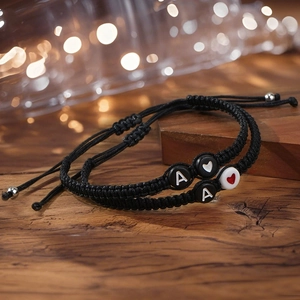 Handmade woven couple bracelets with letter A and heart beads on a rustic wooden table