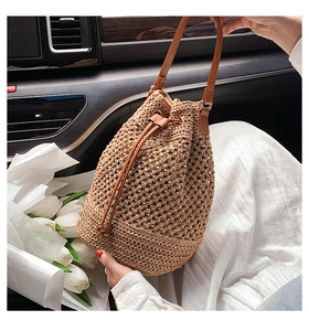 Close-up of woven straw bucket bag with brown leather strap in a lifestyle car setting