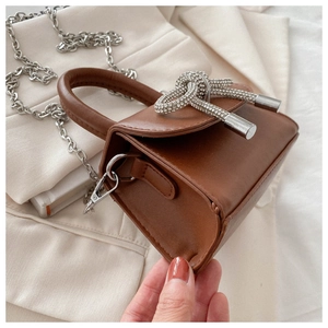 Detail of brown leather mini bag featuring a rhinestone bow buckle and silver chain strap