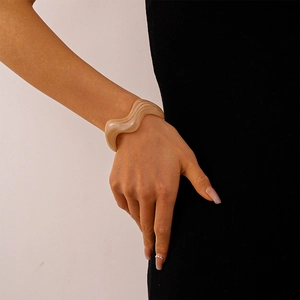 Detailed view of irregular wavy resin bangle featuring sand-colored marble texture
