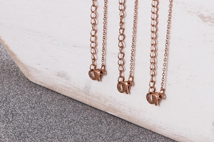 Gros plan de chaînes de collier en or rose avec fermoirs homard sur fond de bois blanc