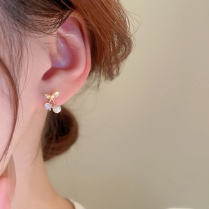 Detailed close-up of cherry-shaped earrings featuring a pearl, zircon, and gold plating