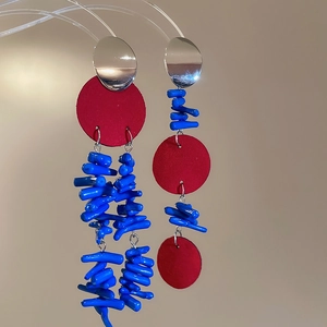 Boucles d'oreilles asymétriques en argent avec disques rouges et perles bleues sur fond beige