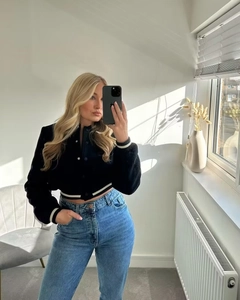 Detail view of a black short baseball jacket with white stripes and high waist denim jeans
