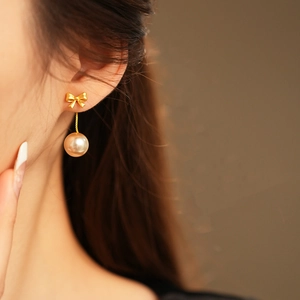 Detail showing elegant gold bow and pearl earrings worn by a model in a natural setting