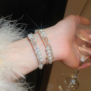 Close-up of multilayer pearl and rhinestone bracelet worn by a model holding a glass